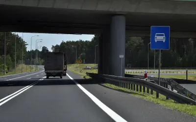 Droga jednojezdniowa pod wiaduktem, z ciężarówką i znakiem informującym o pasie ruchu dla samochodów.