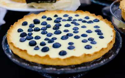 Pyszna tarta z borówkami, z kremowym nadzieniem i chrupiącym spodem, prezentuje się apetycznie na szklanej paterze.