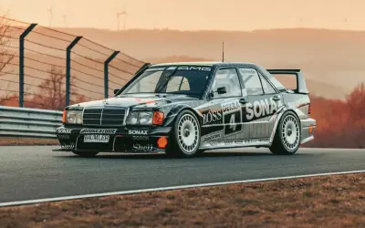 Czarny Mercedes 190 Evo na torze wyścigowym, z licznymi sponsorami na karoserii, gotowy do startu.