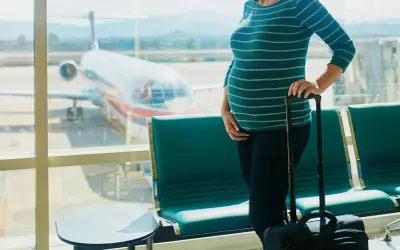 Czekając na lotnisku, przyszła mama zastanawia się, czy w ciąży można latać samolotem. Obok walizka, przed nią samolot.