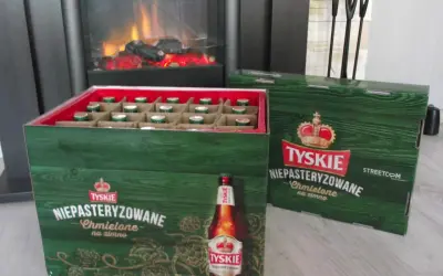 Dwie zielone skrzynki piwa Tyskie Niepasteryzowane Chmielone na zimno stoją obok siebie. W jednej widać rzędy butelek.