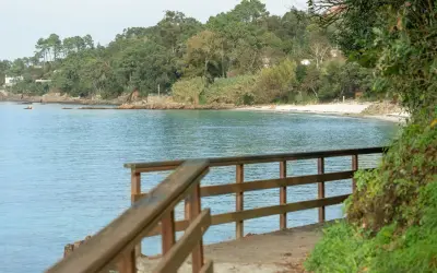 Camino de madera hacia la playa Mogor, con el mar azul y la costa verde al fondo.