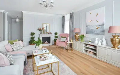 Przytulny pokój w odcieniach pudrowego różu i szarości. Miękka kanapa, różowy fotel i eleganckie meble tworzą harmonijną całość.