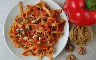 Pyszne spaghetti z papryką i orzechami włoskimi, obok czerwona papryka i surowy makaron.