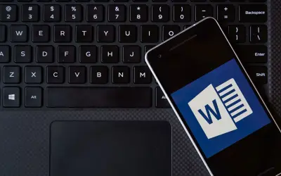 Smartfon z ikoną Worda leży na klawiaturze. Możesz kliknąć ten hiperłącze, aby otworzyć dokument.