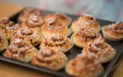 En plåt med nybakade glutenfria kanelbullar, toppade med pärlsocker. Doften av kanel sprider sig i köket.