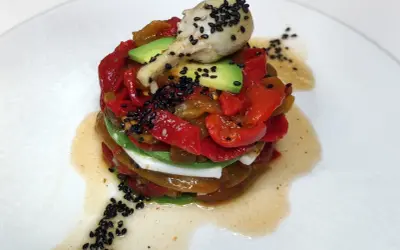 Torre de pimientos del piquillo asados, aguacate y queso fresco, coronada con un alcachofa y semillas de sésamo negro.