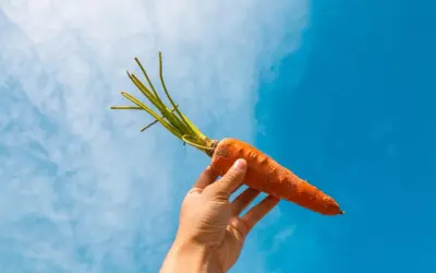 Mano sostiene una zanahoria contra el cielo azul. La zanahoria es un símbolo de salud, ideal para el embarazo.