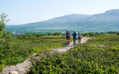 Tre cyklister på stig nära Blåhammaren Storulvån, med fjäll i bakgrunden.