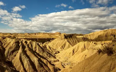 Paisaje árido y erosionado del Desierto de Tabernas, con barrancos y formaciones rocosas bajo un cielo azul con nubes. ¡Un lugar ideal para visitar!