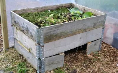 En kompost pallkrage fylld med grönt avfall och jord. Den gamla träkonstruktionen är robust och redo att omvandla trädgårdsrester till näringsrik kompost.
