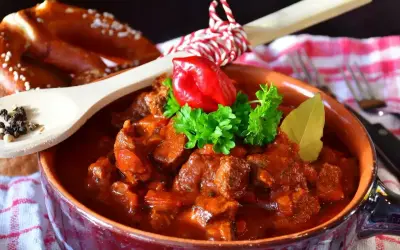 Pyszny gulasz wołowy w glinianej misce, ozdobiony papryczką chili i natką pietruszki. Idealny przepis, jak zrobić gulasz, by zachwycić bliskich.