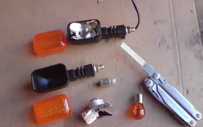 Części do wymiany żarówki kierunkowskazu motocykla: pomarańczowe klosze, obudowy, żarówki, multitool Leatherman Surge.