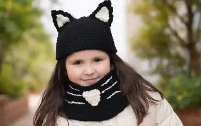 Niña sonriente con un gorro de lana con orejas de gato y bufanda a juego, tejida con agujas.