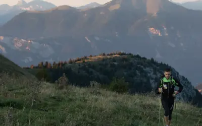 Un coureur en plein effort, bâtons en main, sur un sentier de montagne. Un aperçu de son plan d'entraînement UTMB.