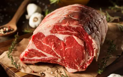 Un succulento pezzo di carne cruda, pronto per diventare un delizioso brasato di manzo. Spezie, erbe aromatiche e aglio completano la scena.