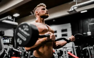 Mężczyzna ćwiczy biceps z ciężarem, wiedząc, że shake proteinowy co daje dla mięśni.