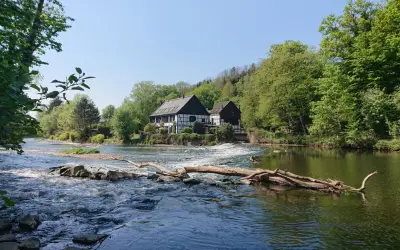 Fachwerkhäuser am Flussufer, wo die **Wipperkotten wandern**. Ein Baumstamm liegt im rauschenden Wasser.