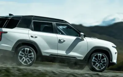 Biały SUV torres auto pokonuje wyboistą drogę, wzbijając tumany kurzu. W tle górzysty, surowy krajobraz.