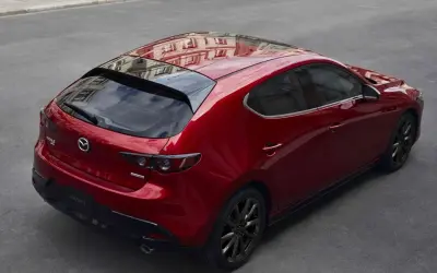 Czerwony Mazda 3 hatchback z czarnymi felgami, odbijający budynki. Elegancki, sportowy design, który odróżnia go od sedana.