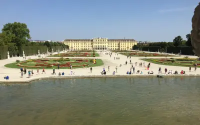 Piękny park w Wiedniu z pałacem w tle i ludźmi spacerującymi po kwiecistych rabatach.