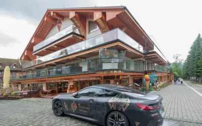 Luksusowy hotel Górski Diament z nowoczesną architekturą i przeszklonymi balkonami. Przed budynkiem stoi elegancki samochód z motywem "Księstwo Góralskie".