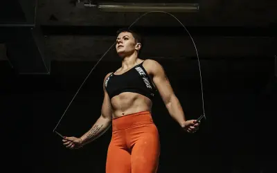 Silna kobieta w sportowym topie i pomarańczowych legginsach skacze na skakance. To świetny trening cardio, który daje siłę i wytrzymałość.