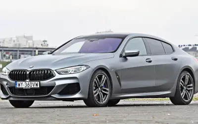 Szary BMW M8 Gran Coupe z czarnym dachem i felgami, zaparkowany na ulicy.