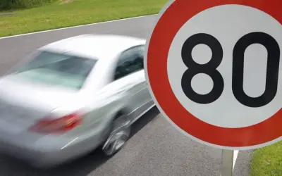 Znak ograniczenia prędkości do 80 km/h. Biały samochód pędzi po drodze, przypominając o przepisach ruchu drogowego i ograniczeniach prędkości w Polsce.