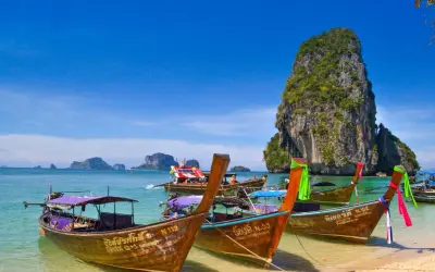 Träbåtar guppar i det turkosa vattnet vid Koh Hong. En imponerande klippa reser sig ur havet.