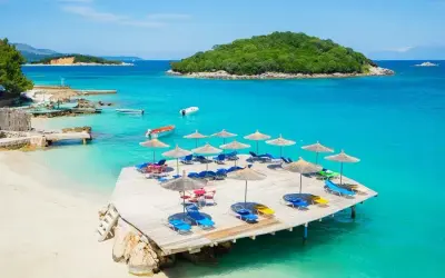 Idealne miejsce, gdzie na wakacje nad morze: piaszczysta plaża, turkusowa woda, leżaki i parasole na drewnianym pomoście.