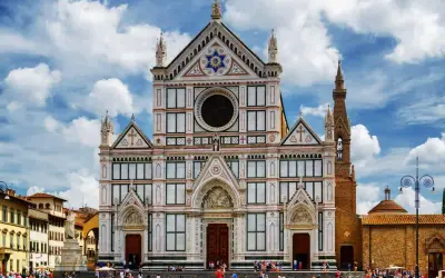 La magnifica facciata della Basilica di Santa Croce domina la piazza, con il cielo azzurro e nuvole bianche.