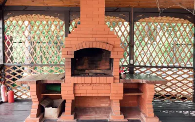 Solidny, prosty grill z cegły w altanie, gotowy na letnie przyjęcia. Obok dwa czerwone gaśnice.