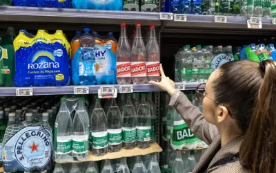 Une femme choisit une bouteille d'eau minérale Badoit. Les étiquettes indiquent la composition et le prix.