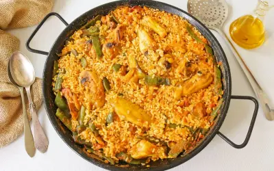 Paella de pollo recién hecha, con trozos de pollo dorado, judías verdes y arroz sabroso en una paellera.