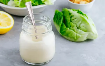 Un pot de vrai sauce césar crémeuse, avec une feuille de laitue romaine et un quartier de citron.