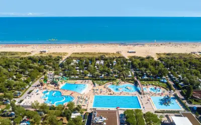 Widok z lotu ptaka na plażę i kompleks basenów w **marina do Venezia**. Widać morze, piaszczystą plażę z leżakami, camping i zjeżdżalnie wodne.