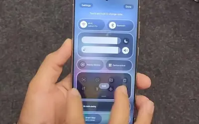 Dłoń steruje smartfonem z interfejsem One UI, pokazując panel szybkich ustawień z Wi-Fi, Bluetooth i innymi opcjami.