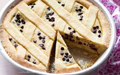 Deliziosa torta ricotta e cioccolato con decorazione a griglia e gocce di cioccolato. Una fetta è stata tolta, rivelando il ripieno cremoso.