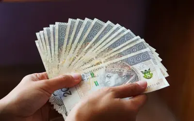 Dłonie trzymają wachlarz banknotów 200 zł. Pieniądze symbolizują świadczenie wspierające, które trafi do potrzebujących.