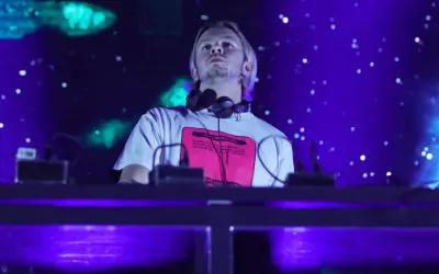 DJ na scenie, w słuchawkach na szyi, z napisem na koszulce. W tle niebieskie światła i efekty. To część lineupu Wisłoujście.