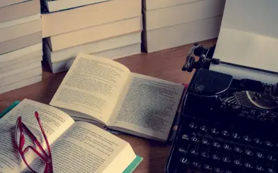 Stos książek, otwarta księga z okularami i zabytkowa maszyna do pisania. Idealne miejsce do tworzenia streszczeń i pisania.