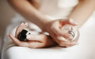 Dłonie kobiety trzymają flakon perfum i czarną nakrętkę. Chcesz wiedzieć, gdzie sprawdzić kod perfum?