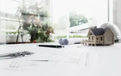 Na stole architekta: makieta domu, cyrkiel, ołówki i plany, które wyznaczają nieprzekraczalna linia zabudowy.