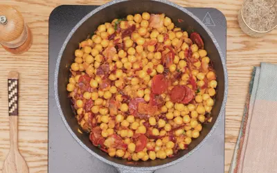 Garbanzos fritos con chorizo y bacon en sartén, listos para servir. Un plato sabroso y reconfortante.