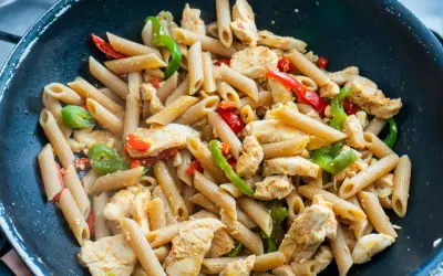 Makaron penne z kurczakiem i papryką w czarnej patelni.