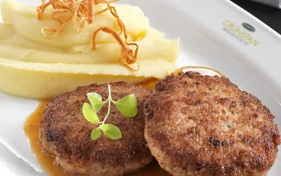 Zwei saftige faschierte Laibchen mit cremigem Kartoffelpüree und knusprigen Röstzwiebeln, garniert mit frischen Kräutern.