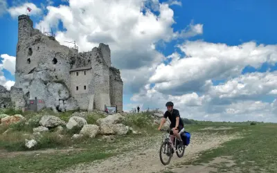 Rowerzysta na szlaku jura krakowsko częstochowska trasa, obok ruin zamku na skale.
