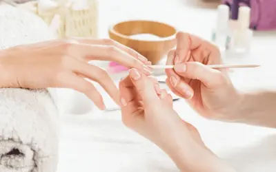 Dłoń przygotowywana do manicure hybrydowego. Delikatne ruchy patyczkiem usuwają skórki, by uniknąć uczulenia na hybrydę.