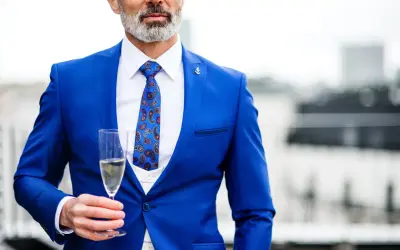 Elegancki mężczyzna w niebieskim stroju koktajlowym z wzorzystym krawatem trzyma kieliszek szampana.